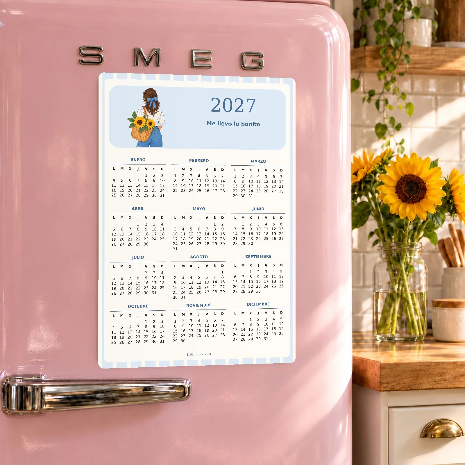 Calendario imantado 2027 Me llevo lo bonito sobre una nevera rosa en una cocina con girasoles.