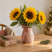 Girasoles en Navidad en una jarra rosa junto a un regalo sobre una mesa de madera.