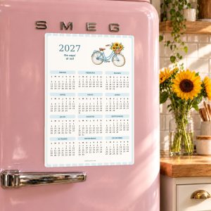Calendario imantado 2027 De aquí al sol sobre una nevera rosa en una cocina con girasoles.
