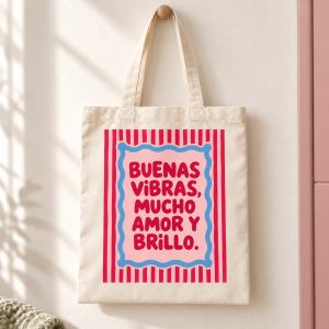 Tote bag de algodón con rayas rosas y rojas, marco azul y la frase Buenas vibras, mucho amor y brillo.