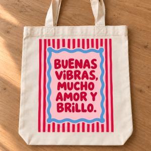 Tote bag de algodón con rayas rosas y rojas, marco azul y la frase Buenas vibras, mucho amor y brillo.